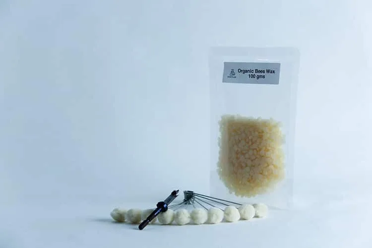 A clear resealable pouch labelled “Organic Bees Wax 100 gms” stands upright with cotton wool balls threaded on a metal tool from the Log dowel inoculation kit mushrooms, set against a plain white background.