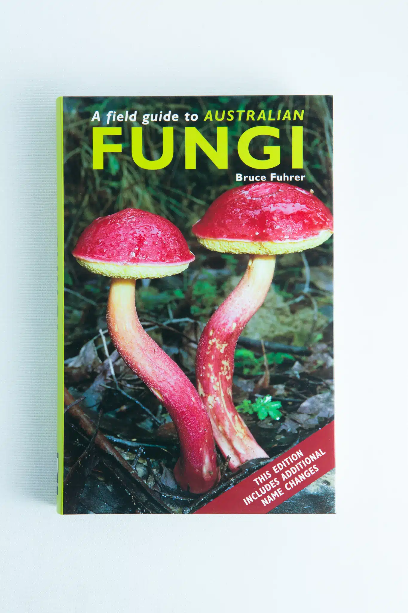 The cover of A Field Guide to Australian Fungi Book by Bruce Fuhrer shows two red-capped mushrooms with yellow stems on the forest floor; this updated edition highlights newly added name changes for key fungi species.