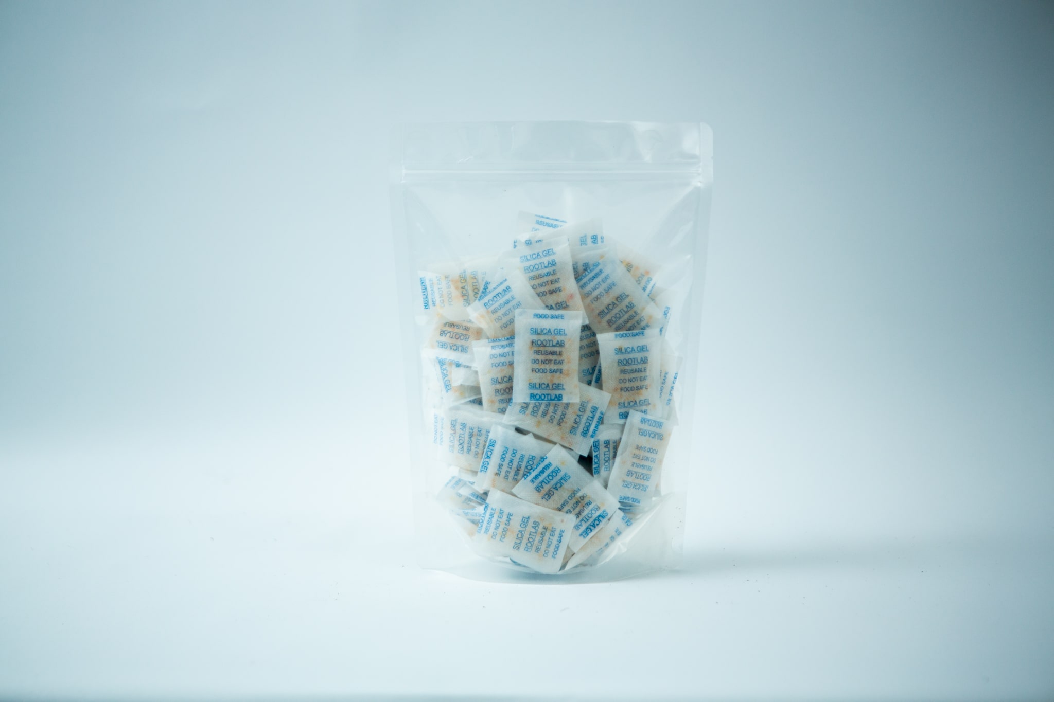 Desiccant Silica Gel 5gm| Reusable 1 A clear plastic bag containing multiple Desiccant Silica Gel 5g | Reusable sachets stands upright against a plain white background. The sachets display blue and white text on their surface.