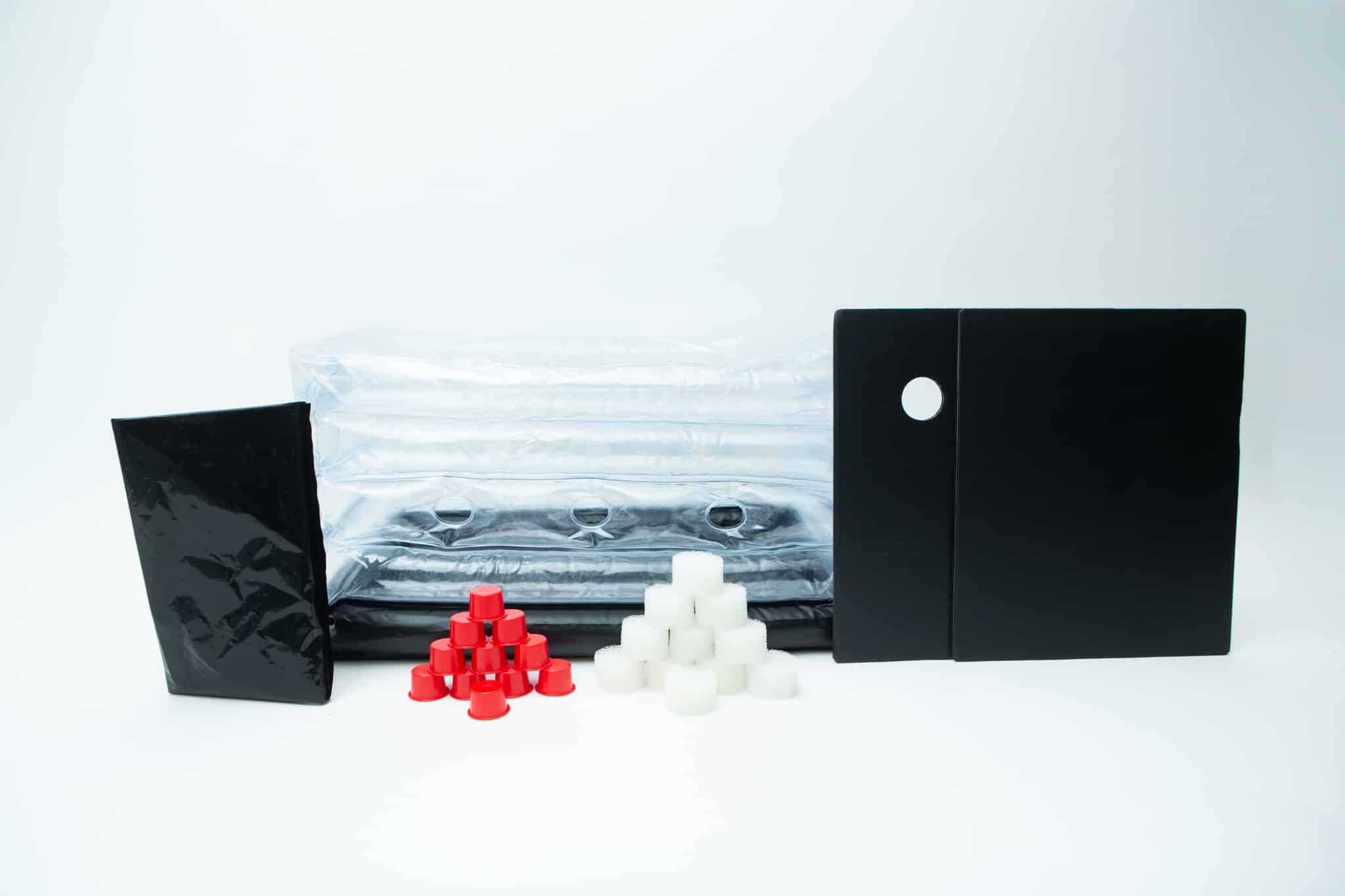 Inflatable monotub kit for Growing mushrooms- Boomer Shroomer V 2.0 1 The Boomer Shroomer V 2.0 Inflatable Monotub Kit for Growing Mushrooms includes black and clear plastic sheets, a black rectangular bag, two ventilated panels, and pyramid-shaped red and white filter plugs—perfect for mushroom cultivation.
