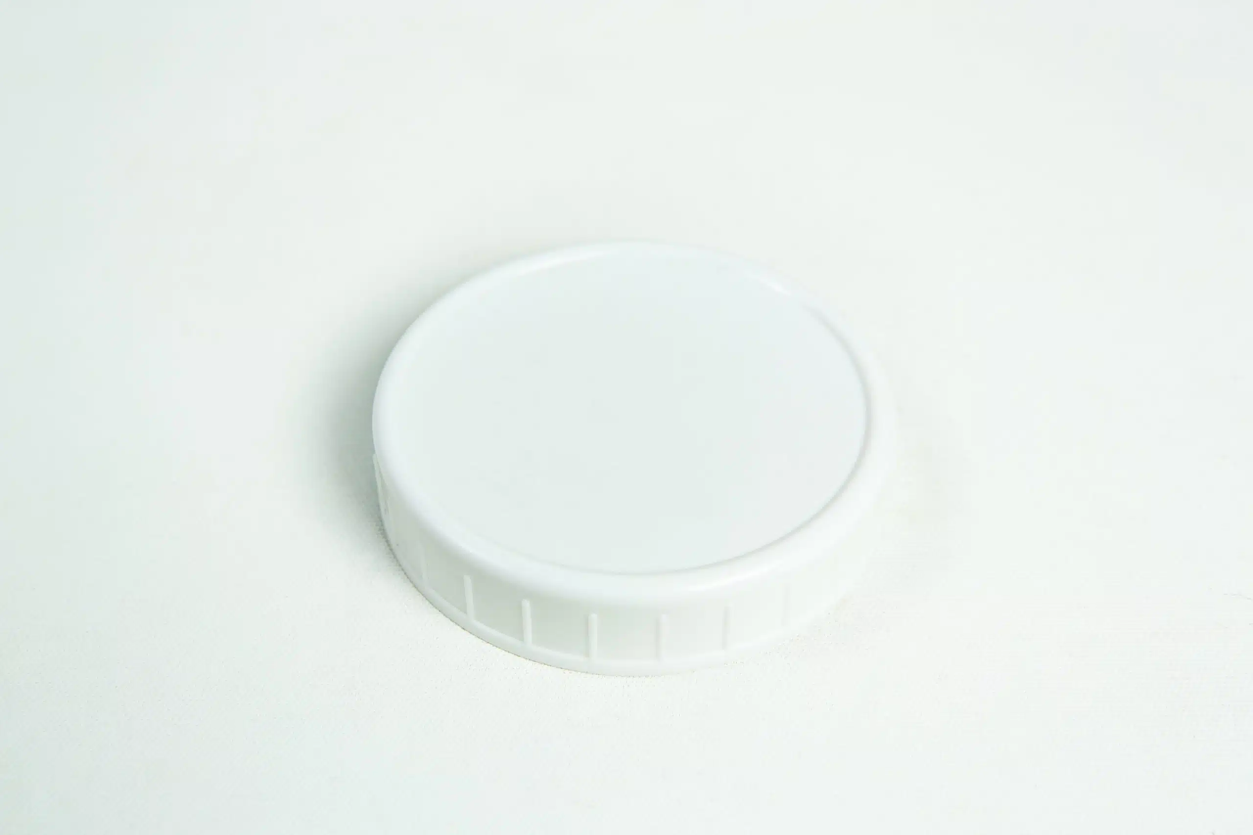 An 86mm Jar Lid from Plain White Plastic Lids rests on a white surface, showcasing its smooth top and ridged sides.