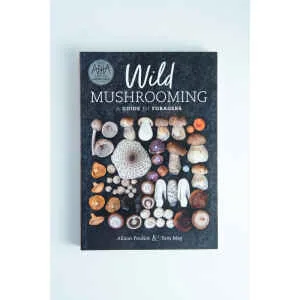 The cover of Wild Mushrooming: A Guide for Foragers Book by Alison Pouliot and Tom May displays rows of assorted mushrooms on a white background, reflecting the spirit of wild mushrooming.