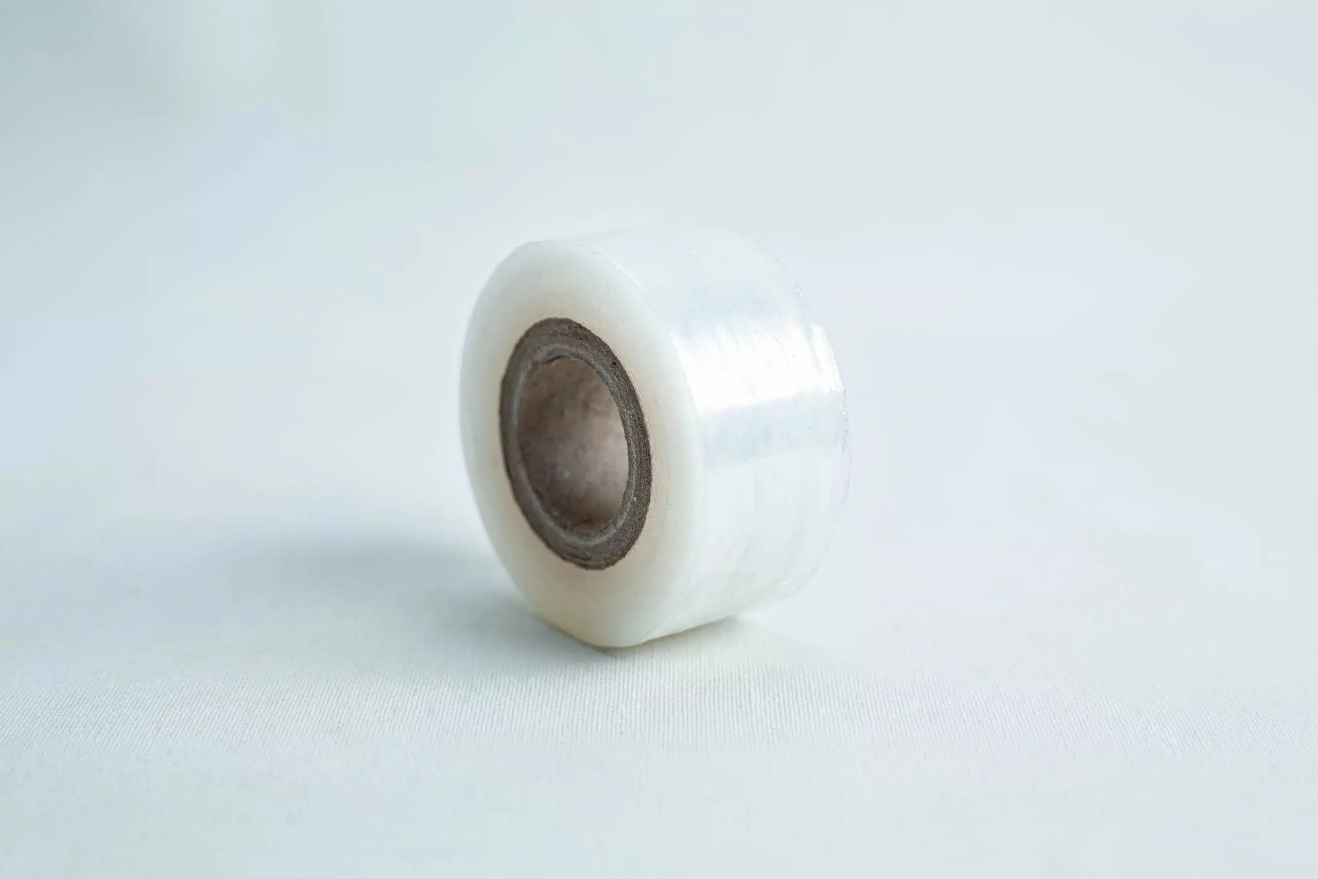 A roll of Grafting Tape to seal agar plates, clear with a brown cardboard core, stands upright on a light surface against a pale background—ideal for sealing delicate samples or agar plates.
