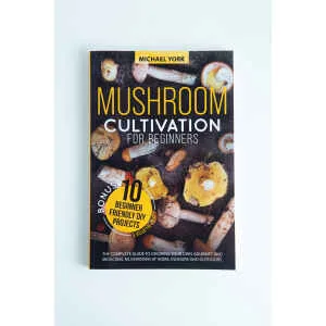 The book "Mushroom Cultivation for Beginners: The Complete Guide to Growing Your Own Gourmet and Medicinal Mushrooms at Home, Indoors and Outdoors" lies on a white surface, its cover featuring mushrooms and 10 beginner-friendly DIY projects.