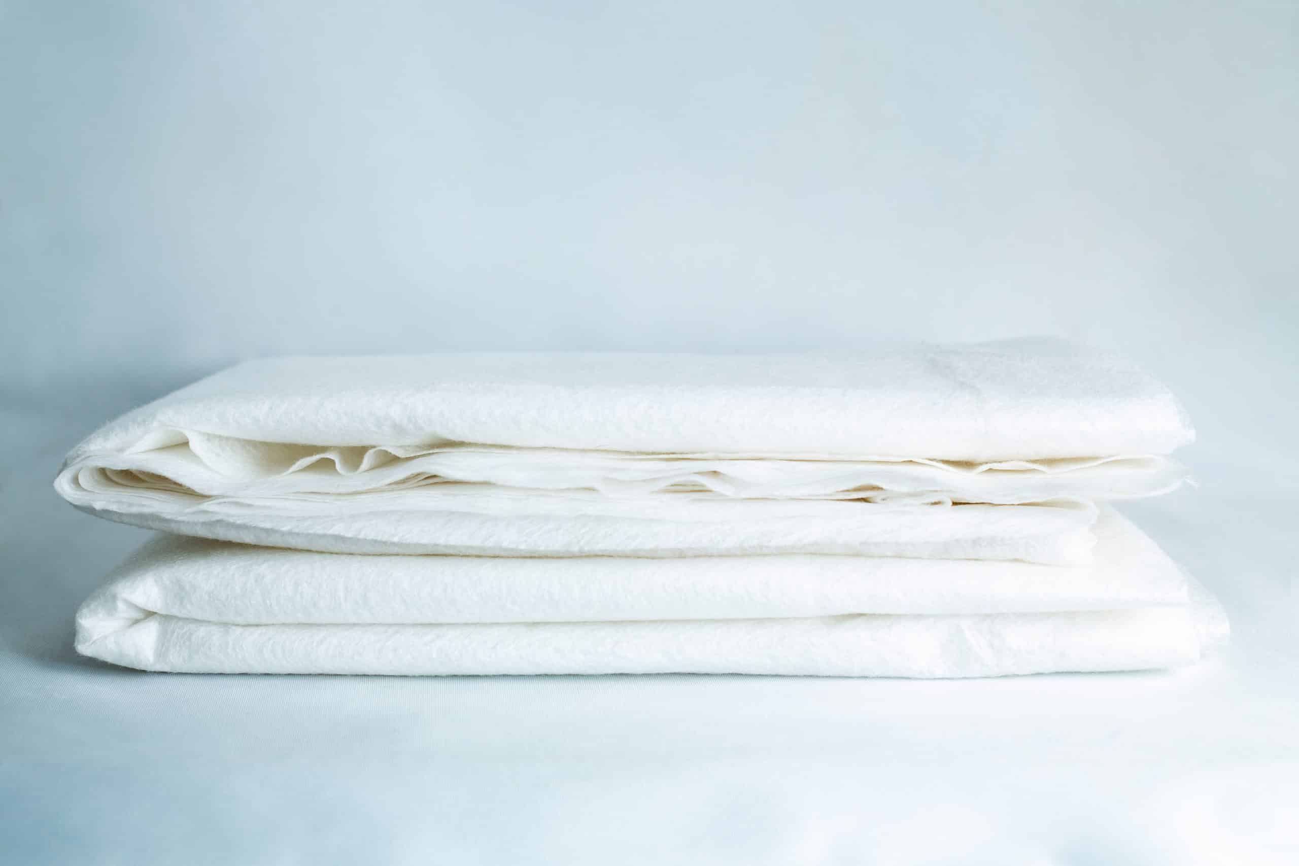 Light Log Blanket 1 A stack of two folded white Log Blankets sits on a white surface against a light background.