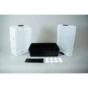 Home 17 A black plastic max yield bin is positioned between two clear lidded containers, all standing upright. In front of the bin are a black packet, a small black item, and several white circular pads arranged in a row—ideal for mushroom growing.