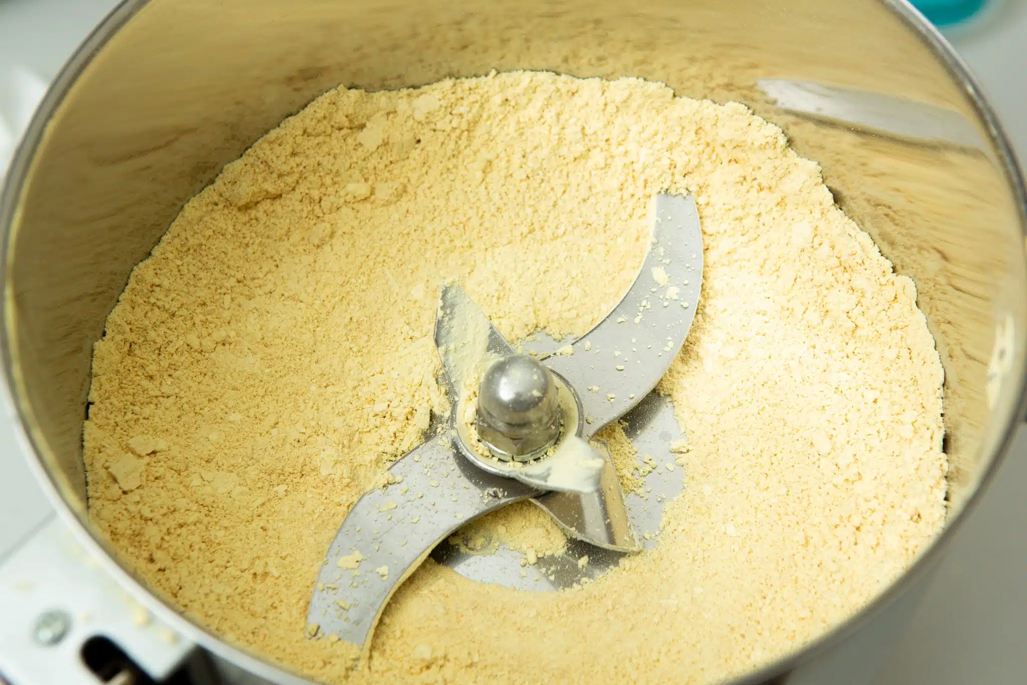 Australian grown Freeze Dried Lions Mane Mushroom (Powder) 4 Close-up of a metal food processor bowl containing finely ground yellow powder with metal blades in the centre.