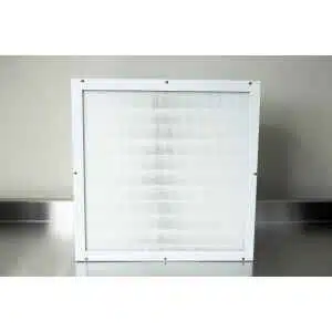 A square HEPA air filter (H14) with a white metal frame and fine mesh sits upright on a stainless steel surface against a plain light-coloured wall, ideal for use in a Laminar Flow Hood.