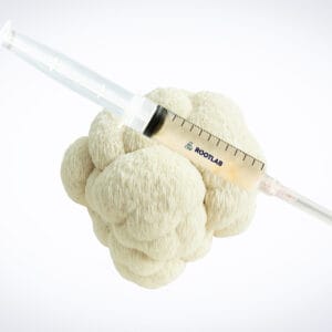 A syringe filled with a pale liquid rests on top of a head of cauliflower against a plain white background.