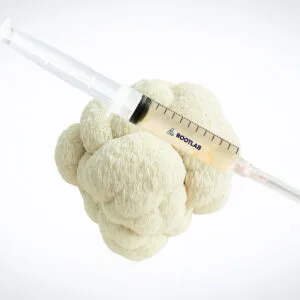 A plastic syringe filled with a light-coloured liquid rests on top of a cauliflower head, set against a plain white background.