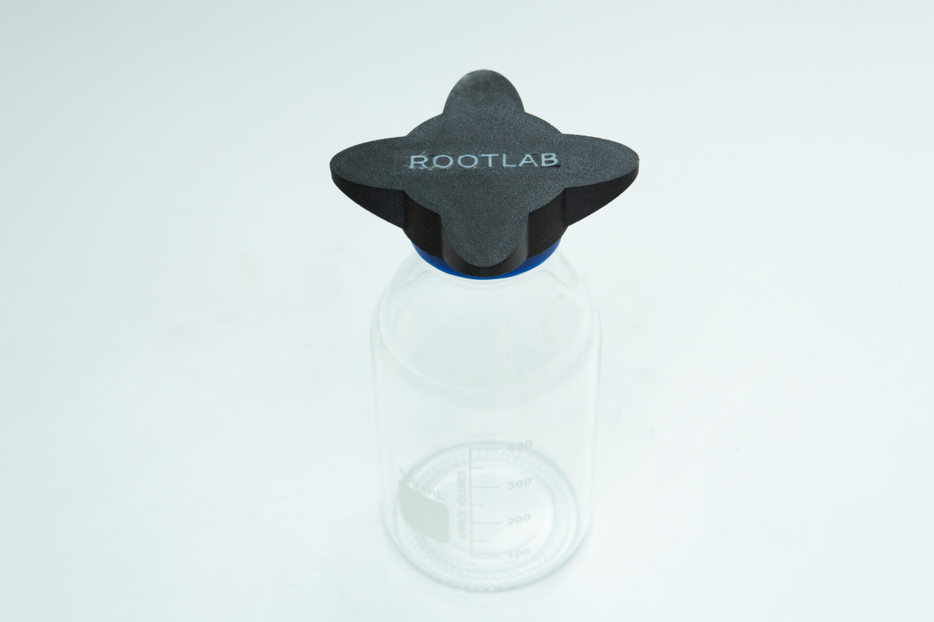 Reagent Bottle Cap Wrench | Rootlab Original | 3D Printed 6 A clear glass laboratory bottle with volume markings and a black, cross-shaped lid labelled ROOTLAB sits on a white surface.