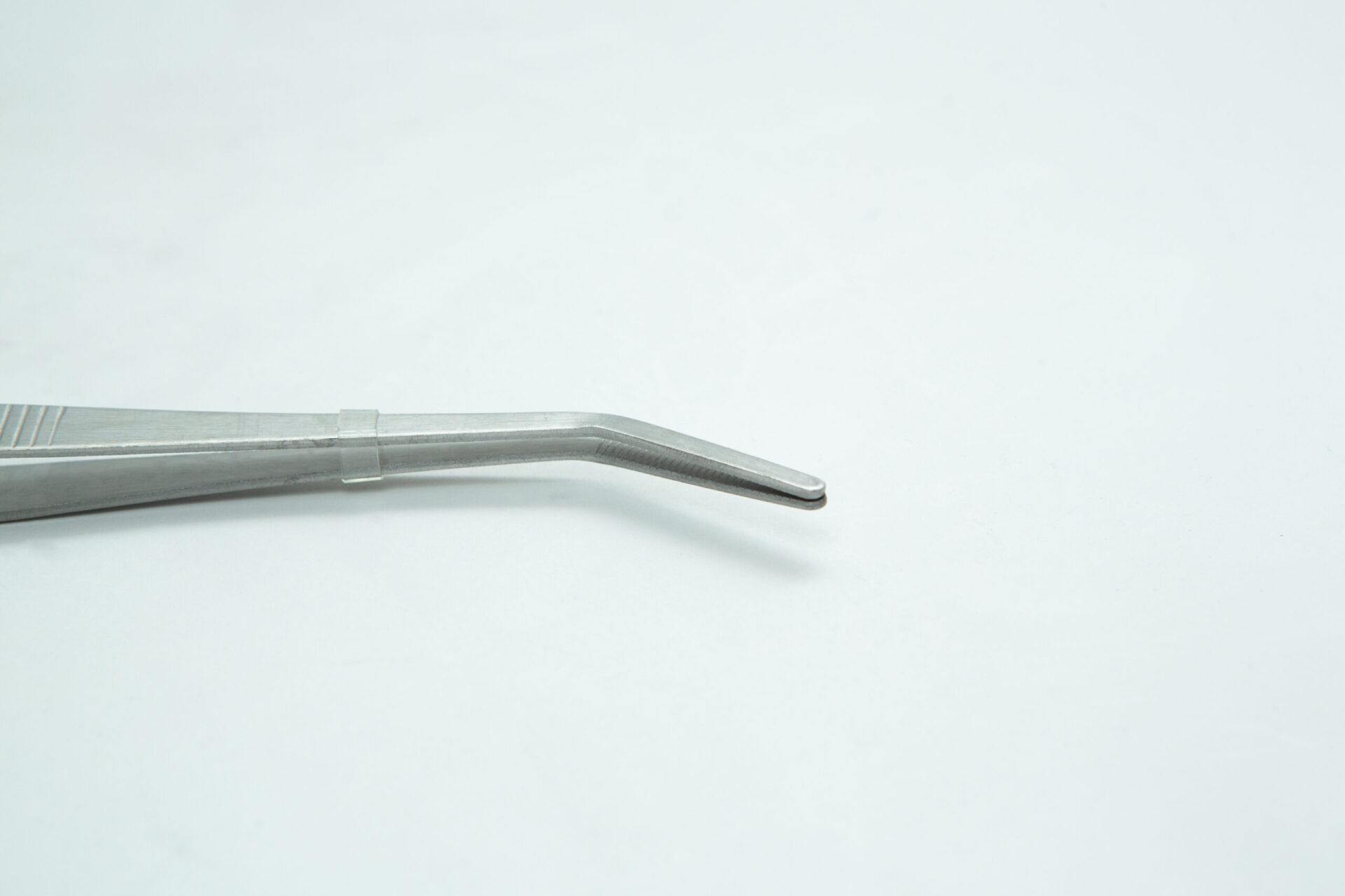 Stainless Steel Plant tissue culture Lab Forceps | Curved & Straight Tips | 15cm 3 A close-up of a metal tweezer with a bent tip resting on a plain white surface. The background is minimal and uncluttered.
