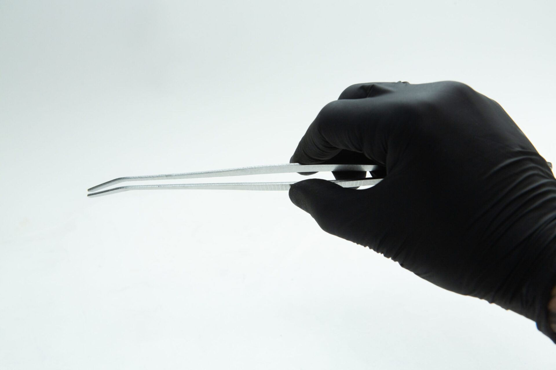 Stainless Steel Plant tissue culture Lab Forceps | Curved & Straight Tips | 25cm 5 A hand wearing a black glove holds a pair of metal forceps with a bent tip against a plain white background.