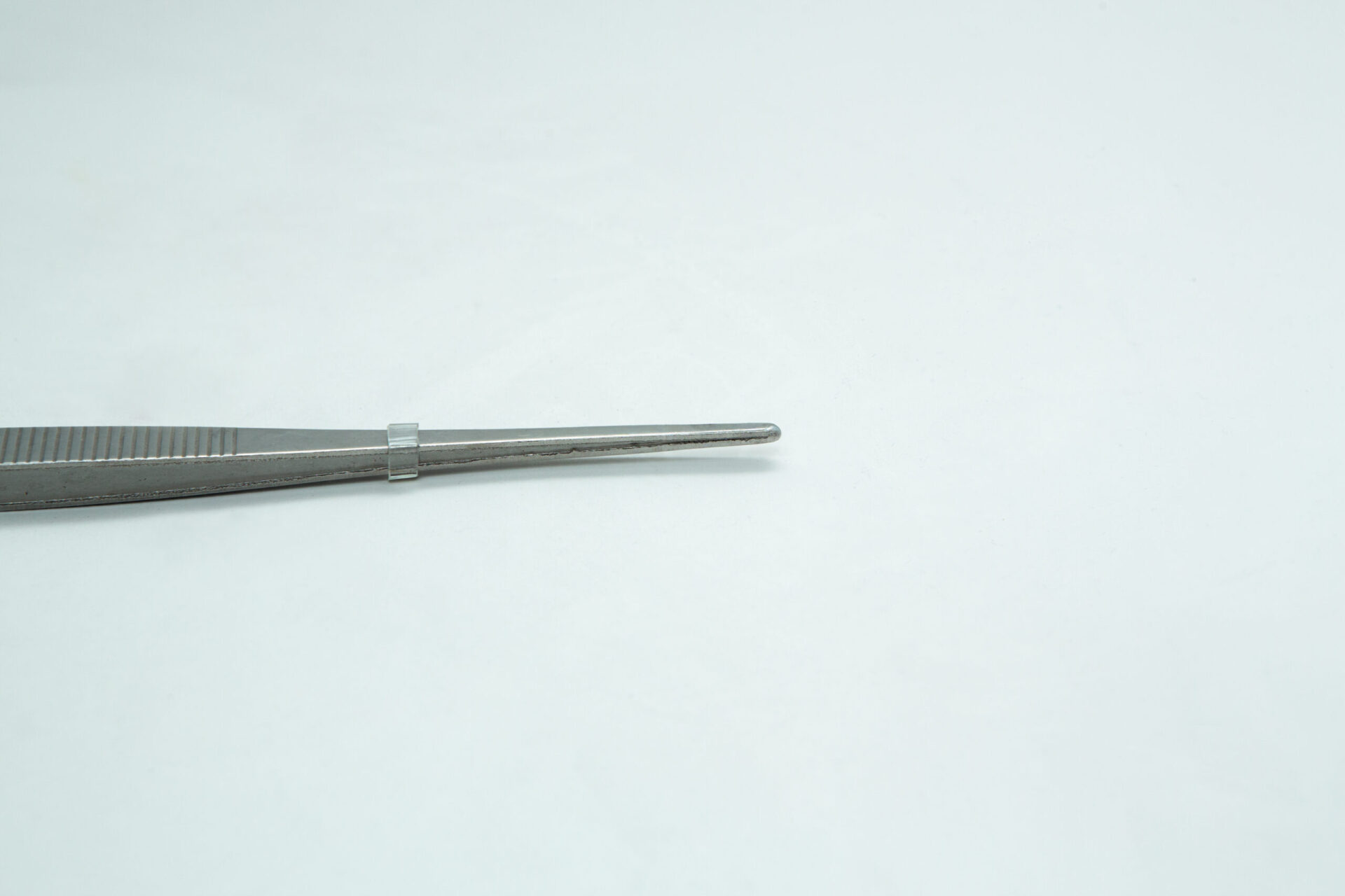 Stainless Steel Plant tissue culture Lab Forceps | Curved & Straight Tips | 25cm 7 A close-up of a metal tweezer placed horizontally on a plain white background, with only the tips and part of the handle visible on the left side.