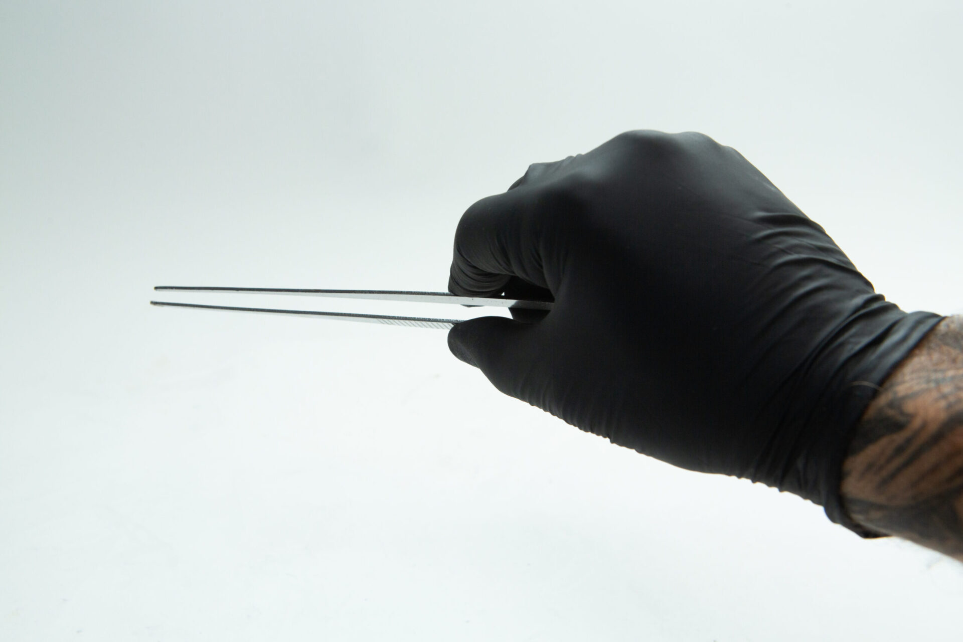Stainless Steel Plant tissue culture Lab Forceps | Curved & Straight Tips | 25cm 8 A person wearing a black latex glove holds a pair of tweezers against a plain white background. The person's wrist and part of a tattoo on their arm are visible.