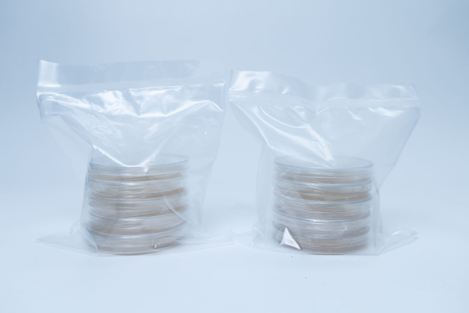 5 x Agar Plates (MEA) and 5 x Agar Plates (MEAG) Pre poured 90mm 2 Two stacks of petri dishes with brownish contents are sealed in clear plastic bags and placed on a white surface against a plain background.