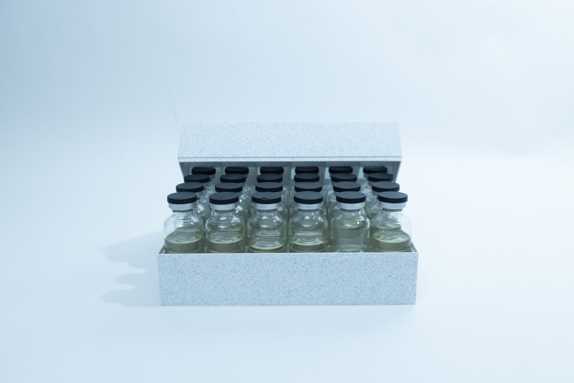 Sterile Liquid Culture Vials, Dr Myc Adaptive LC, Crimp Sealed 25 A box containing 24 clear glass vials with black caps is open and arranged in four rows on a white surface with a light blue background.