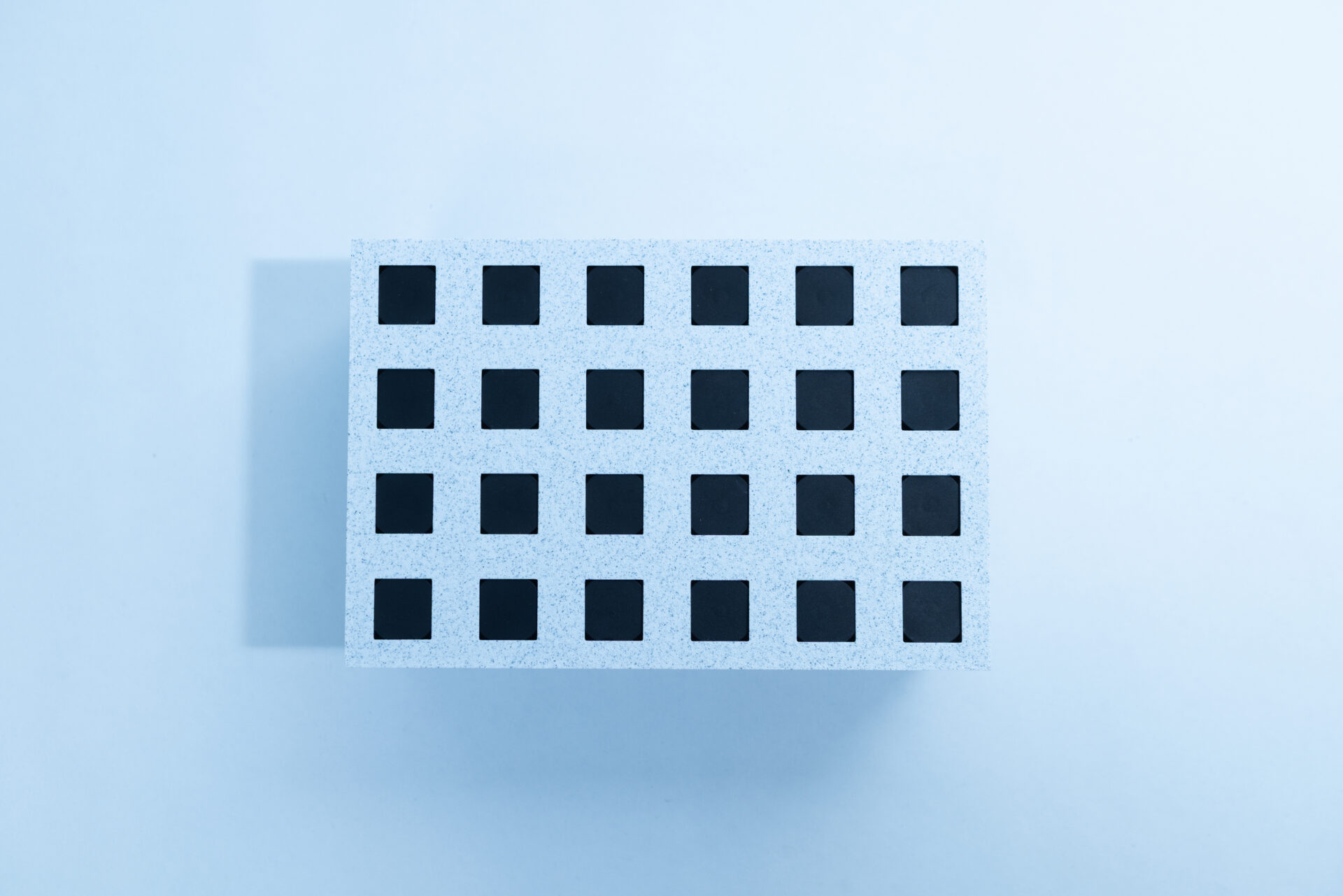 Sterile Liquid Culture Vials, Dr Myc Adaptive LC, Crimp Sealed 26 A rectangular object with a grid of 24 square holes arranged in four rows and six columns, photographed from above against a plain, light blue background. The object casts a shadow to the left.