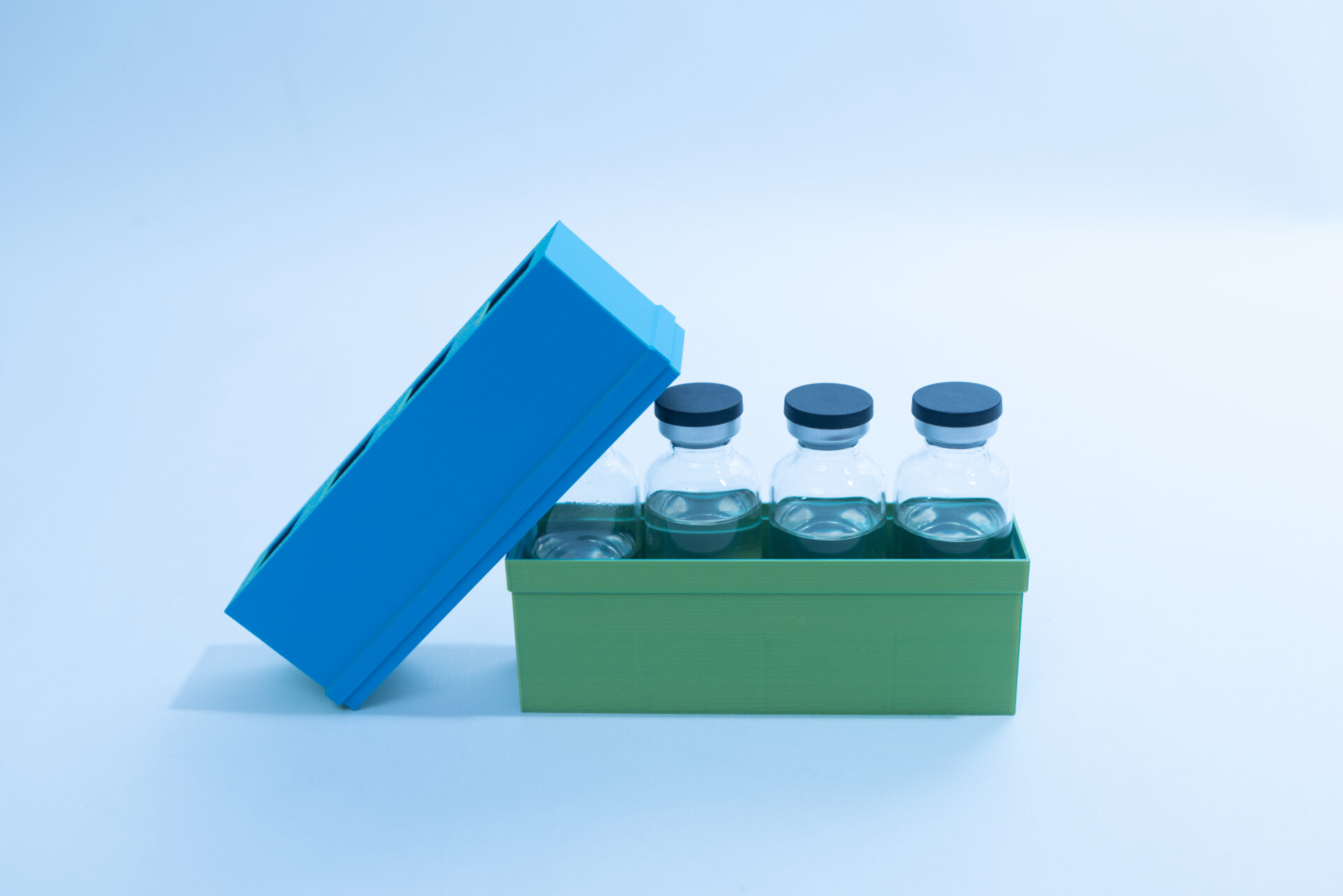 Sterile Liquid Culture Vials, Dr Myc Adaptive LC, Crimp Sealed 29 Four glass vials with black caps are placed in a green container with a partially open blue lid. The container is set against a plain, light blue background.