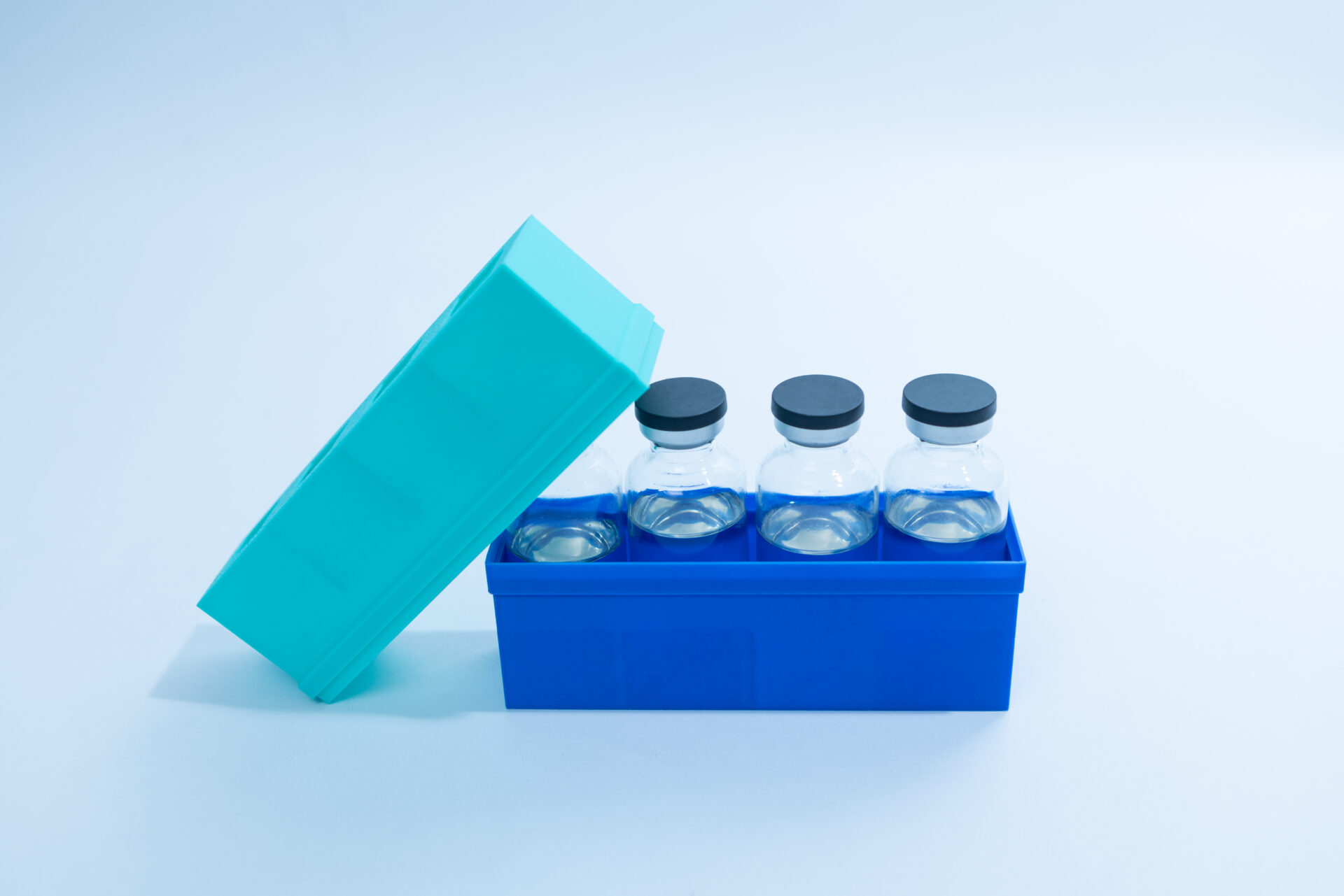 Sterile Liquid Culture Vials, Dr Myc Adaptive LC, Crimp Sealed 30 Four glass vials with black caps are placed in a blue plastic container with an open light blue lid. The background is plain white.