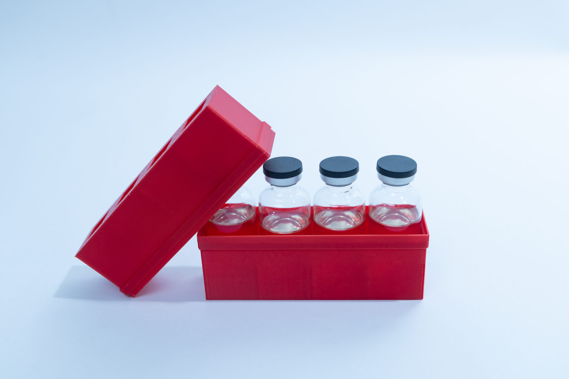 Sterile Liquid Culture Vials, Dr Myc Adaptive LC, Crimp Sealed 23 Three clear glass vials with black caps are placed in a red plastic container. The container's lid is partially open, revealing the vials inside. The background is plain and light-coloured.
