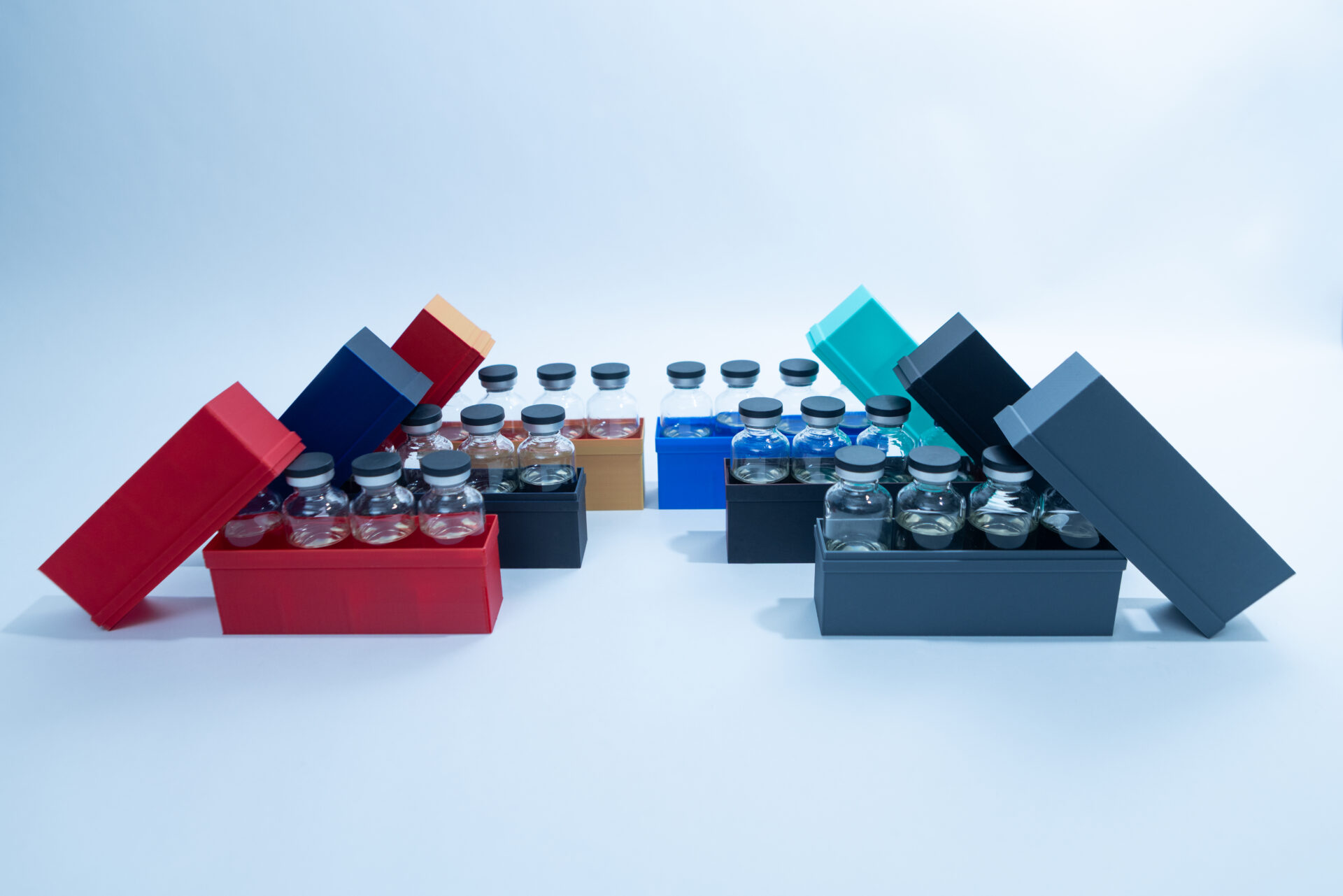 Sterile Liquid Culture Vials, Dr Myc Adaptive LC, Crimp Sealed 31 Nine rectangular boxes in various colours are open, each containing several clear glass vials with black caps. The boxes are arranged in three rows on a plain light background.