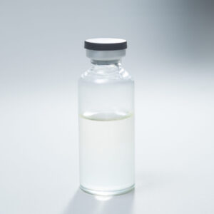 Home 10 A clear glass vial with a grey rubber stopper is filled halfway with a transparent liquid. The vial is placed on a plain, light-coloured surface with a soft shadow beneath it.