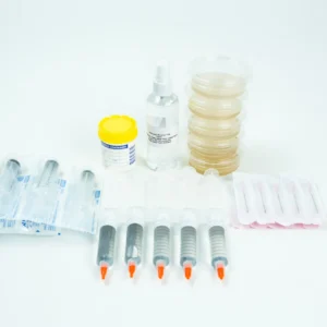 Several sealed medical syringes, a yellow-capped specimen container, a clear spray bottle, stacked Petri dishes, and packaged items are arranged on a white surface.