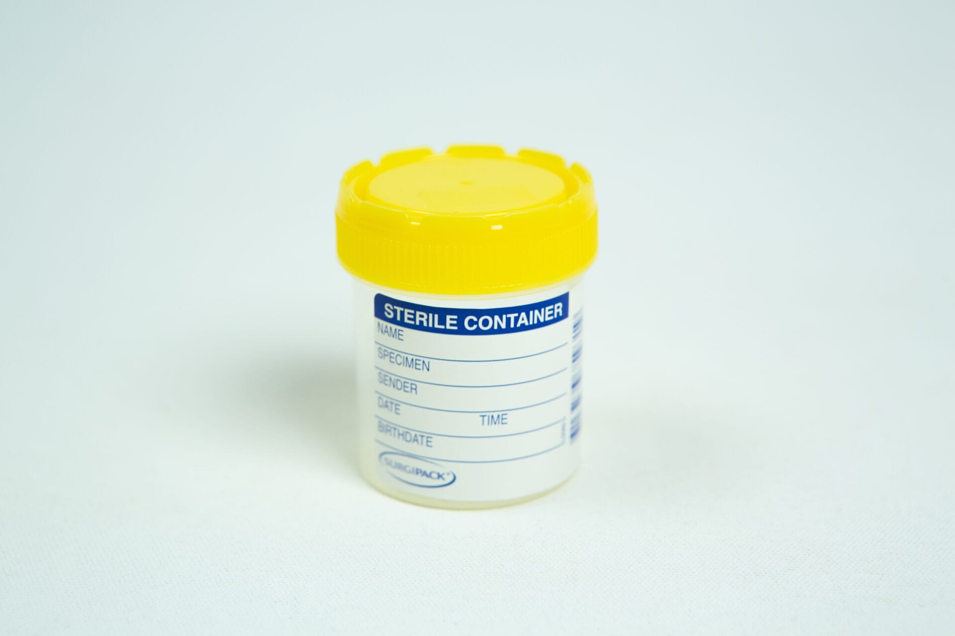 Spore Print to Spore syringe transfer Kit 2 A transparent plastic sterile specimen container with a yellow lid sits on a white surface. The label on the container has blank fields for name, specimen, provider, date, and time.