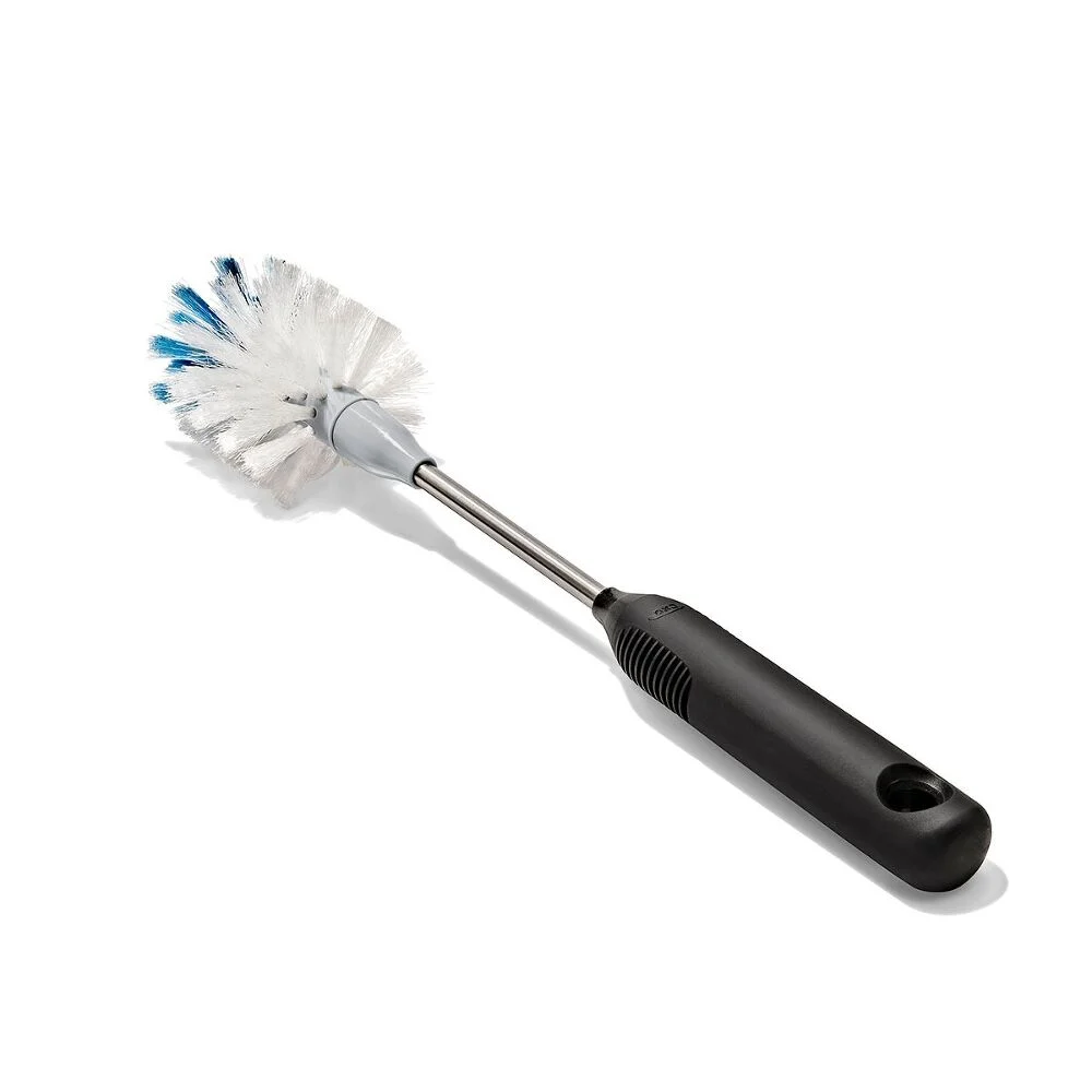 OXO Good Grip Stainless Steel Bottle Brush with replaceable head 2 A bottle brush with a round white bristle head, featuring a few blue bristles, attached to a metal shaft and a black plastic handle with a hole at the end, set against a white background.