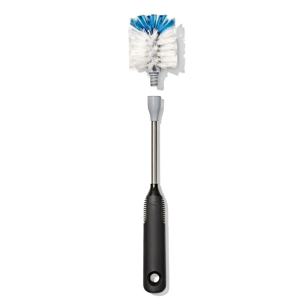 OXO Good Grip Stainless Steel Bottle Brush with replaceable head 3 A bottle brush with a black handle, silver neck, and white bristles tipped with blue at the end. The bristle head is cylindrical and mounted on a detachable section of the handle.